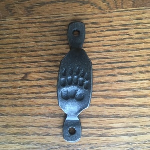 May include: Black metal bear paw pull handle. The handle is shaped like a bear paw print and has two holes for mounting.