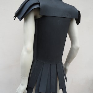 May include: A black sleeveless garment with a layered, pleated skirt and a high collar. The garment has a geometric design with sharp angles and a futuristic aesthetic.
