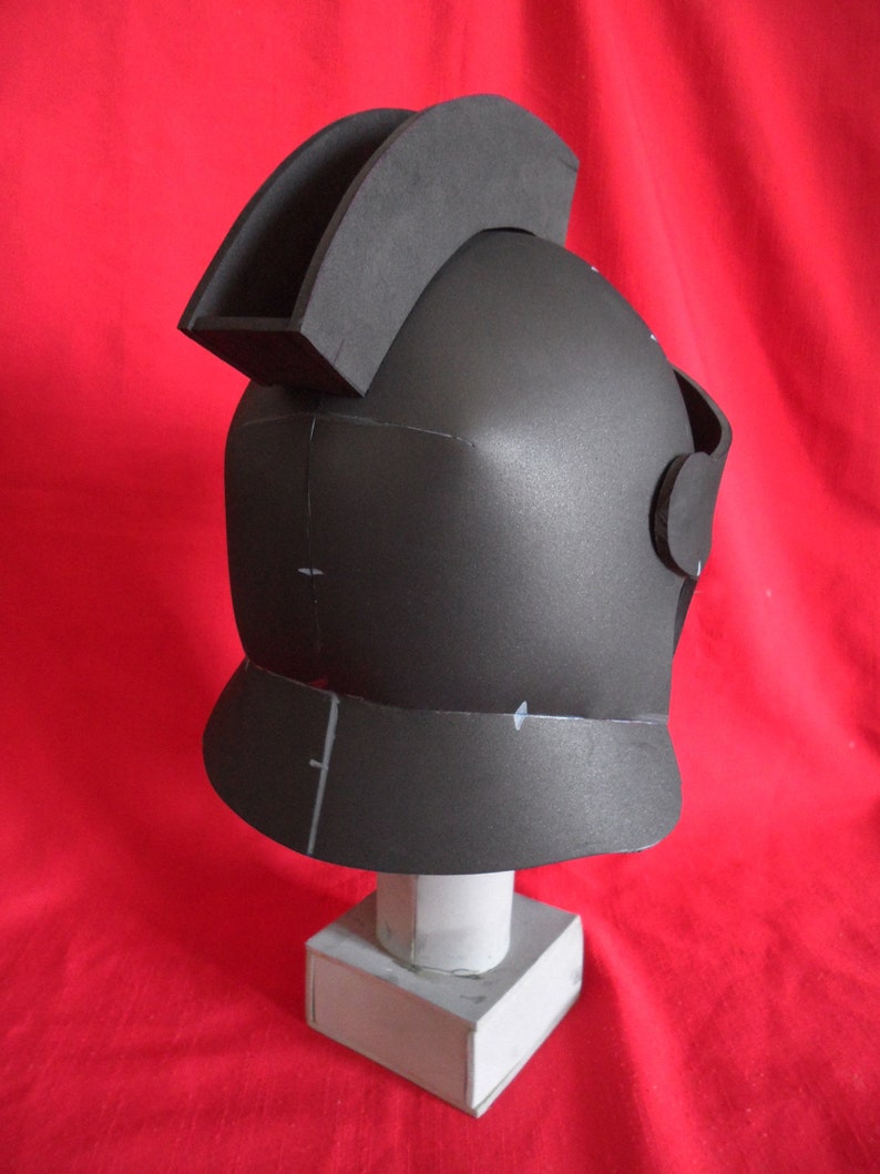 May include: A black foam helmet with a raised crest on top. The helmet is sitting on a white pedestal.