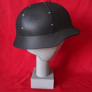 May include: A black helmet with white markings on a red background. The helmet has a rounded top and a brim that curves down around the sides.