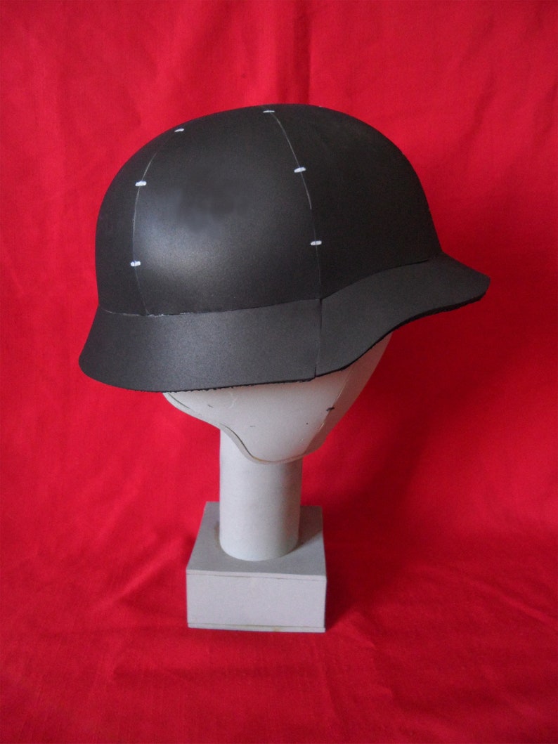 May include: A black helmet with white markings on a red background. The helmet has a rounded top and a brim that curves down around the sides.
