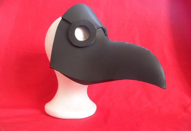 May include: A black leather plague doctor mask with a long beak and a round eye hole. The mask is on a white mannequin head.