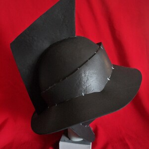 May include: A black helmet with a pointed top and a wide brim. The helmet is made of a textured material and has a simple design.