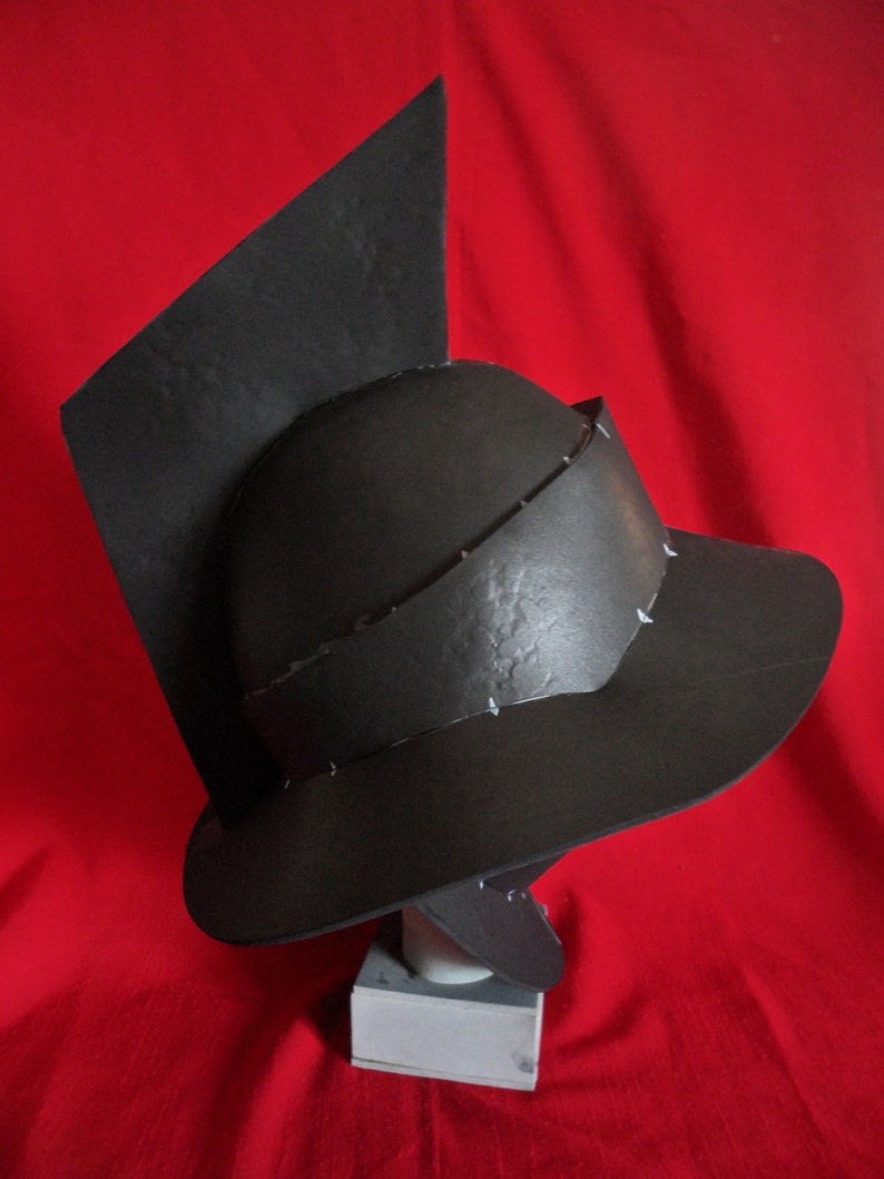 May include: A black helmet with a pointed top and a wide brim. The helmet is made of a textured material and has a simple design.