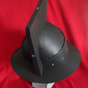 May include: A black helmet with a pointed top and a wide brim. The helmet is made of cardboard and has a textured surface.