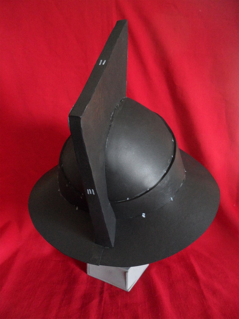 May include: A black helmet with a pointed top and a wide brim. The helmet is made of cardboard and has a textured surface.