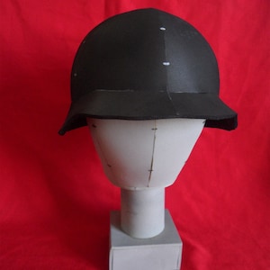 May include: A black helmet with a wide brim, made of foam, on a white mannequin head. The helmet is on a white base.