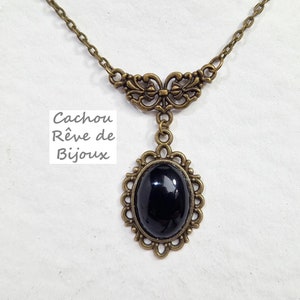 May include: A black oval pendant necklace with an ornate bronze frame. The chain is also bronze and has a delicate floral design.