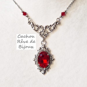 Könnte beinhalten: Eine silberne Halskette mit einem roten Edelstein-Anhänger. Der Anhänger ist von einem verzierten silbernen Rahmen umgeben. Die Halskette hat eine zarte Kette mit kleinen roten Kristallen.