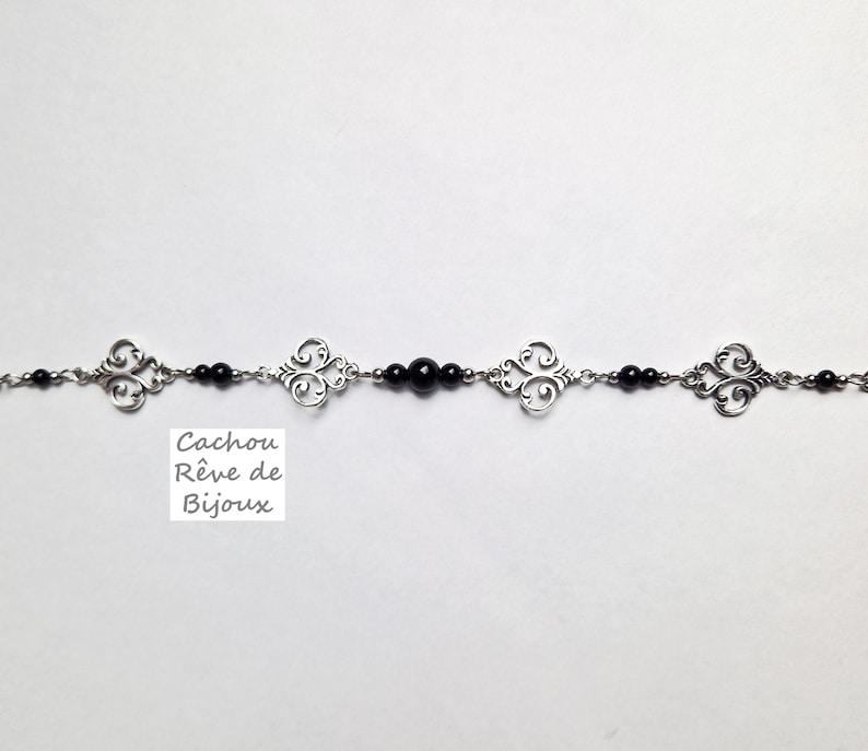 May include: A silver chain bracelet with black beads and decorative silver charms. The bracelet has a tag that reads "Cachou R&ecirc;ve de Bijoux".