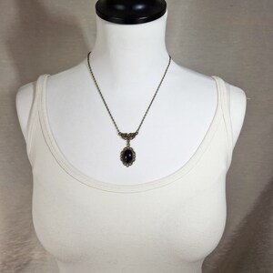 May include: A black oval gemstone pendant necklace with a bronze chain and ornate bronze detailing.