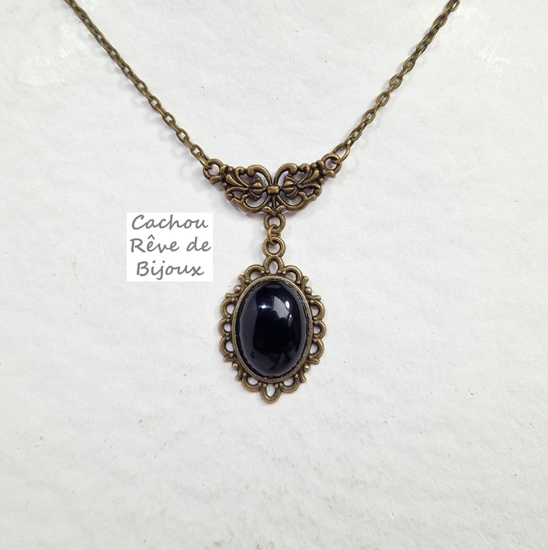 May include: A black oval pendant necklace with an ornate bronze frame. The chain is also bronze and has a delicate floral design.