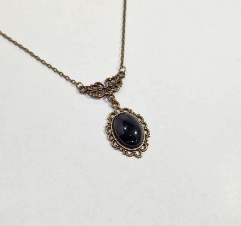 May include: A delicate gold necklace with a black oval gemstone pendant. The pendant is surrounded by an ornate, filigree design.