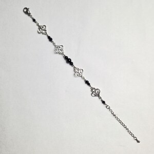 May include: A silver chain bracelet with black beads and silver filigree charms.