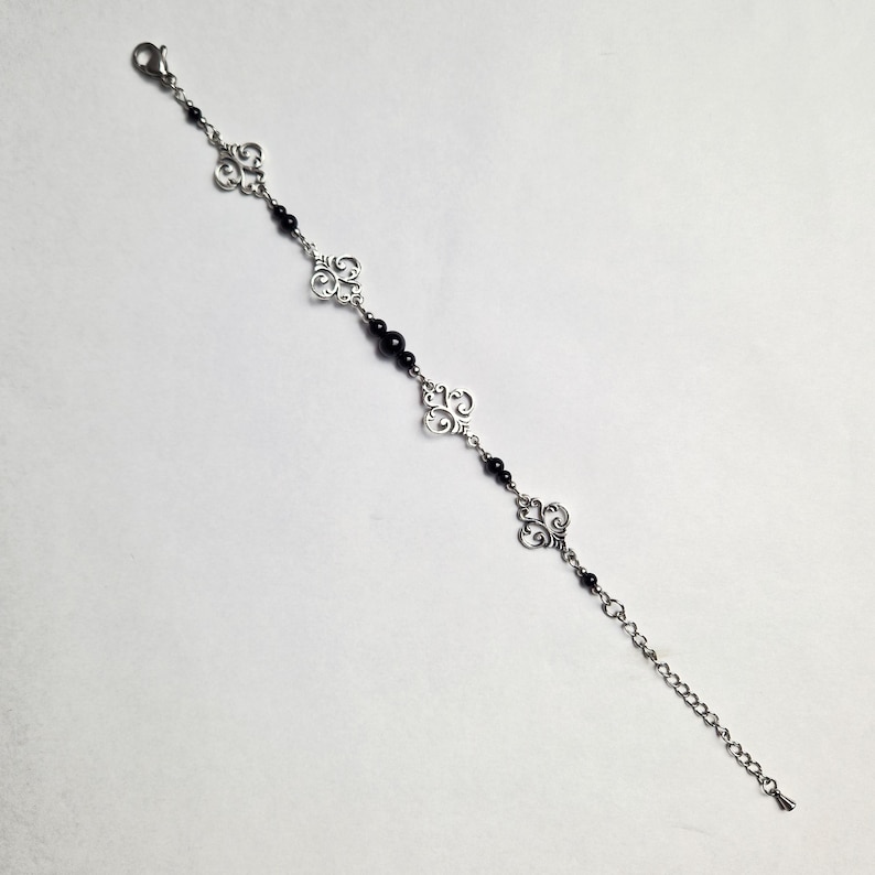 May include: A silver chain bracelet with black beads and silver filigree charms.