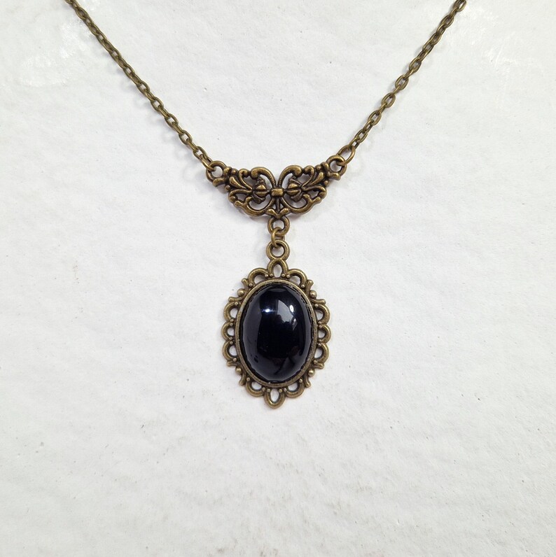May include: A black gemstone pendant necklace with an ornate bronze setting. The necklace features a delicate chain and a decorative bronze bail.