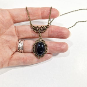 May include: A black oval pendant necklace with a bronze chain and ornate bronze filigree detailing. The pendant features a black oval stone set in a bronze frame.