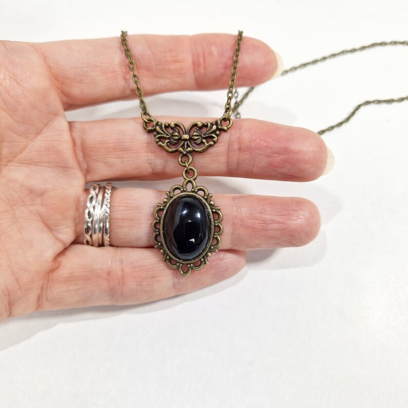 May include: A black oval pendant necklace with a bronze chain and ornate bronze filigree detailing. The pendant features a black oval stone set in a bronze frame.