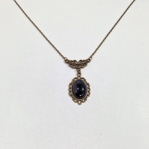 May include: A delicate gold necklace with a black oval gemstone pendant set in an ornate frame.
