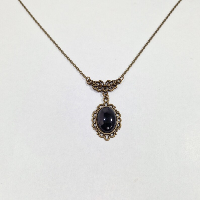 May include: A delicate gold necklace with a black oval gemstone pendant set in an ornate frame.