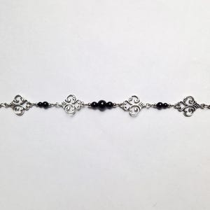 May include: A silver chain bracelet with black beads and decorative silver charms.