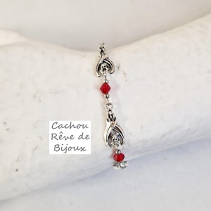 Könnte beinhalten: Silberarmband mit roten Kristallperlen und einem Fledermaus-Anhänger. Das Armband liegt auf einer weißen Oberfläche. Cachou Rêve de Bijoux steht auf einem weißen Quadrat.
