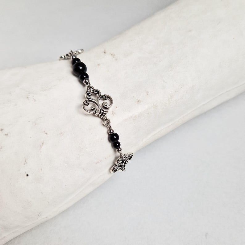 May include: A silver chain bracelet with black beads and decorative silver charms. The charms are in the shape of a stylized heart.