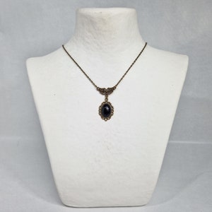 May include: A delicate gold necklace with a black oval gemstone pendant. The pendant is surrounded by a detailed filigree design.