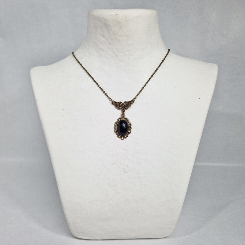 May include: A delicate gold necklace with a black oval gemstone pendant. The pendant is surrounded by a detailed filigree design.