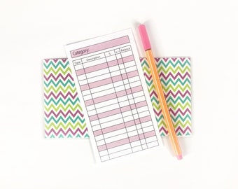 Puede incluir: Un rastreador de presupuesto imprimible blanco con columnas para la fecha, la descripción, la cantidad y el saldo. El rastreador está sobre una superficie blanca con un papel estampado en chevron rosa y verde y un resaltador rosa y naranja.