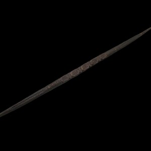 May include: A long, slender, dark brown wooden rod featuring intricate, repeating carved patterns along its central section. The rod tapers to a fine point at one end and has a slightly curved, hooked tip at the other, showcasing detailed craftsmanship.
