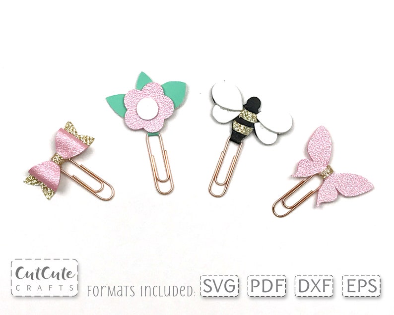 Op de afbeelding: Vier decoratieve paperclips met verschillende ontwerpen: een roze strik, een roze bloem met groene bladeren, een zwart-witte bij en een roze vlinder. De clips zijn goudkleurig.