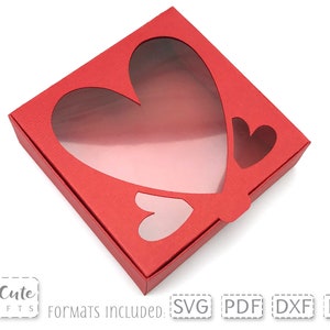 May include: Red cardboard box with a heart-shaped window. The box is designed for Valentine's Day gifts or favors.