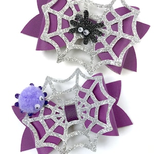Op de afbeelding: Twee paarse en zilveren glitter spinnenweb strikken met een spin op elk. De strikken zijn voor het knutselen en maken deel uit van een SVG strik sjabloon. "Spider Web Bow" en "SVG Bow Template" staan onder de strikken.