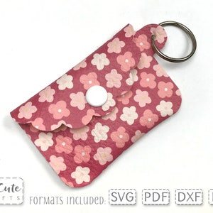 May include: A pink leather keychain with a floral pattern and a white button closure. The keychain has a silver key ring.