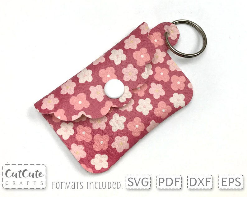 May include: A pink leather keychain with a floral pattern and a white button closure. The keychain has a silver key ring.