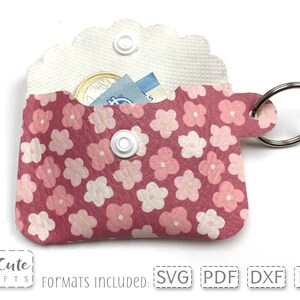 May include: Pink leather keychain with a floral pattern and a small pocket for holding cash and coins. The keychain has a silver ring and a white snap button.