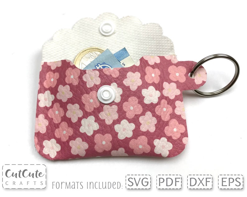 May include: Pink leather keychain with a floral pattern and a small pocket for holding cash and coins. The keychain has a silver ring and a white snap button.