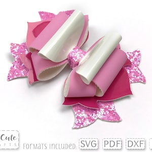 Puede incluir: Lazo de capas rosa y blanco con detalles de purpurina. El lazo está hecho de fieltro y tiene un centro blanco. El lazo está sobre un fondo blanco.