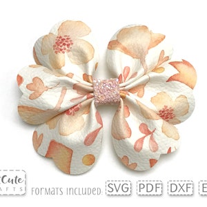 May include: A white faux leather bow with a watercolor floral pattern in shades of peach, pink, and yellow. The bow has a sparkly pink center and is perfect for adding a touch of whimsy to any project.