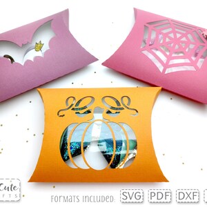 May include: Three pillow boxes with cut-out designs for Halloween. The boxes are pink, orange, and purple. The designs are a bat, a spider web, and a pumpkin. The text "Formats Included: SVG PDF DXF EPS" is at the bottom of the image.