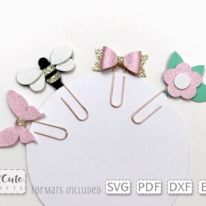 Op de afbeelding: Vier paperclip-toppers met een bij, vlinder, strik en bloem ontwerp. De toppers zijn roze, wit, groen en gouden glitter. De paperclips zijn goud.