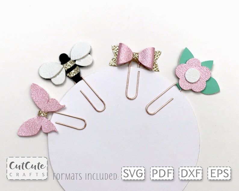 Op de afbeelding: Vier paperclip-toppers met een bij, vlinder, strik en bloem ontwerp. De toppers zijn roze, wit, groen en gouden glitter. De paperclips zijn goud.