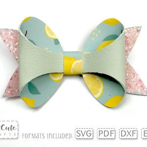 May include: A light green faux leather bow with a lemon print. The bow has pink glitter accents on the ends.