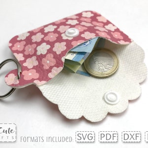 May include: A pink and white floral patterned key chain wallet with a white snap closure and a silver key ring. The wallet is open and has a few bills and a coin inside.