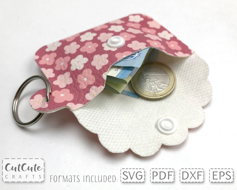 May include: A pink and white floral patterned key chain wallet with a white snap closure and a silver key ring. The wallet is open and has a few bills and a coin inside.