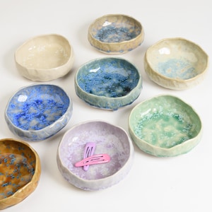 May include: Eight small ceramic bowls in various colours and patterns. The bowls have a textured, uneven surface and are perfect for holding small items like jewellery or trinkets.
