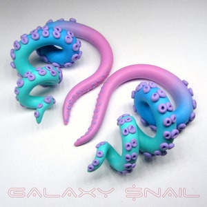 May include: A pair of galaxy-themed ear gauges, one is a light blue to pink gradient and the other is a turquoise to purple gradient. Both are shaped like an octopus tentacle with purple bumps.
