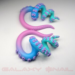 May include: A pair of galaxy-themed ear gauges, one pink and blue, the other blue and green, with a swirling octopus design and purple accents.  The gauges are made of polymer clay and are shaped like a spiral.