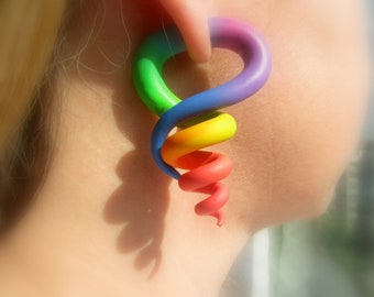May include: A rainbow-colored spiral ear gauge made of polymer clay. The gauge is in the shape of a snail and is worn in a person's ear.
